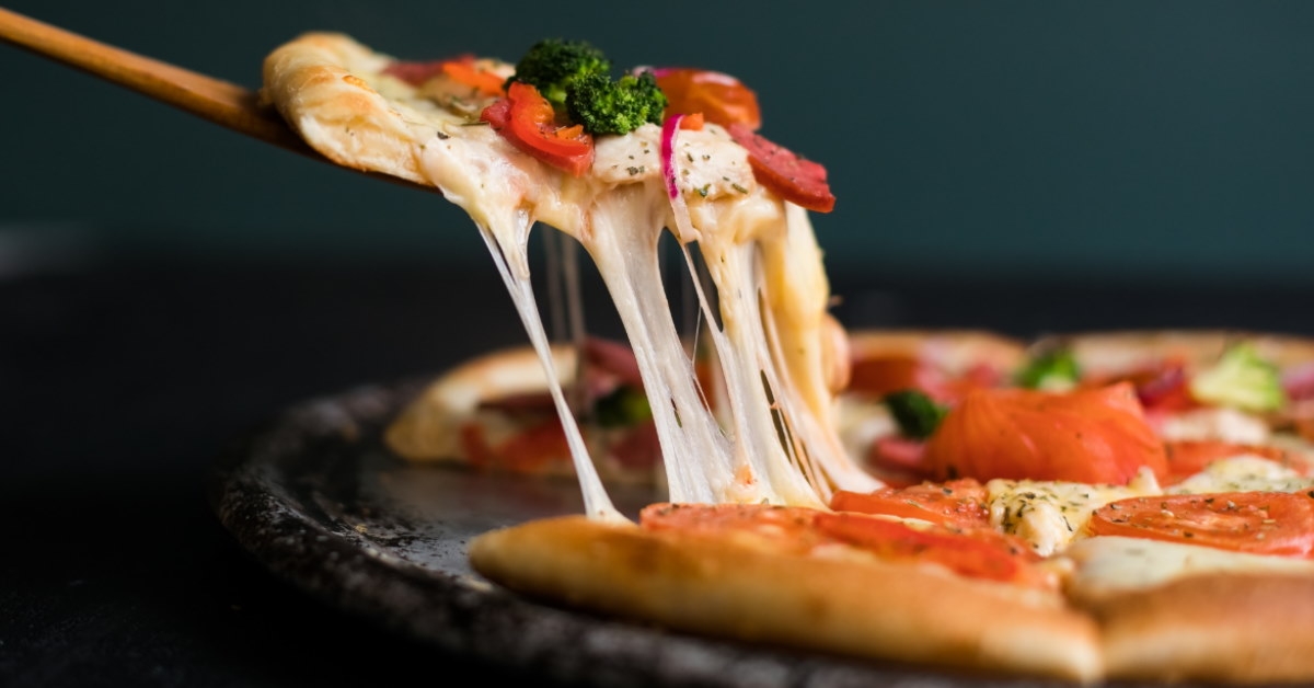 slice of fresh pizza with strings of melted cheese being pulled apart using a wooden ladle