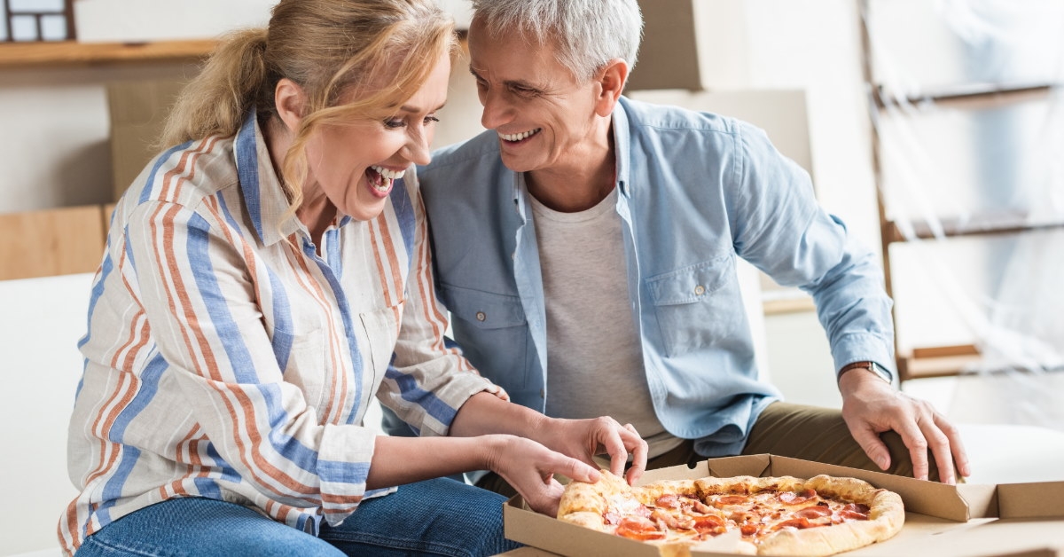 senior couple sitting in couch eating pizza together