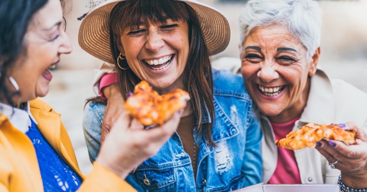 senior women sitting on the street, eating pizza, and laughing joyfully together