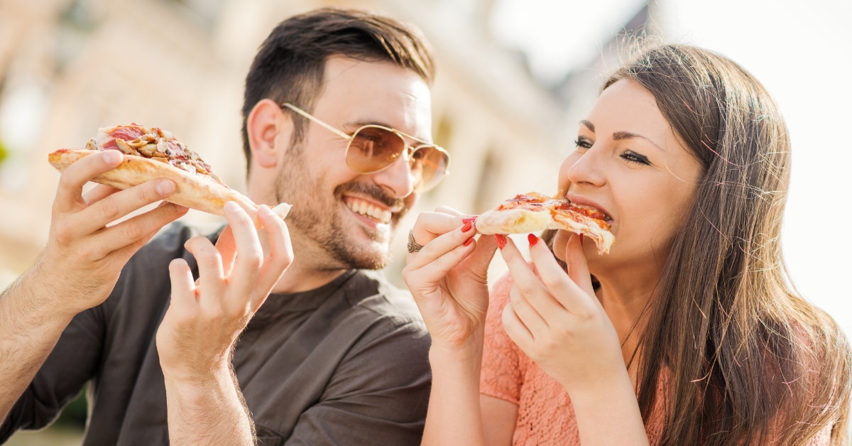 young couple enjoying pizza together outdoors 