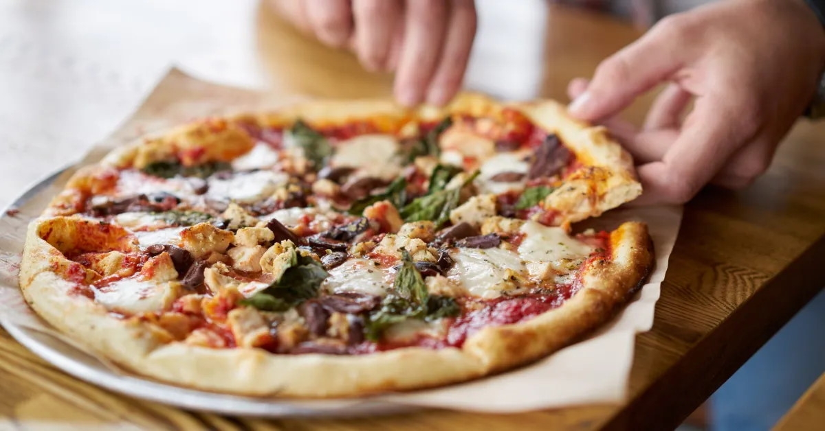 man in a restaurant taking out a slice of pizza on a wooden table