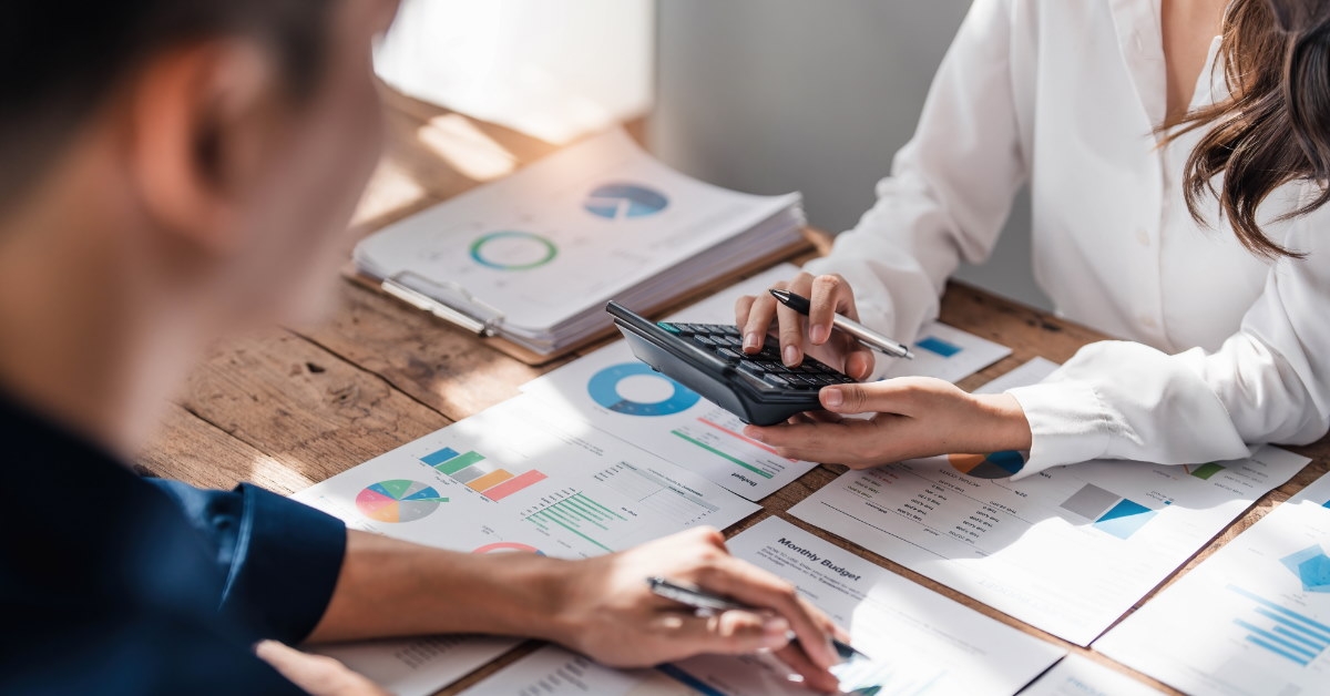colleagues sitting at table with colorful project plans on table while using calculator