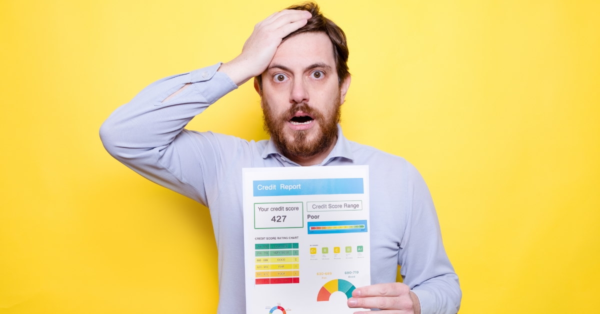 man standing in front of yellow background holding head in stress at poor credit score on piece of paper