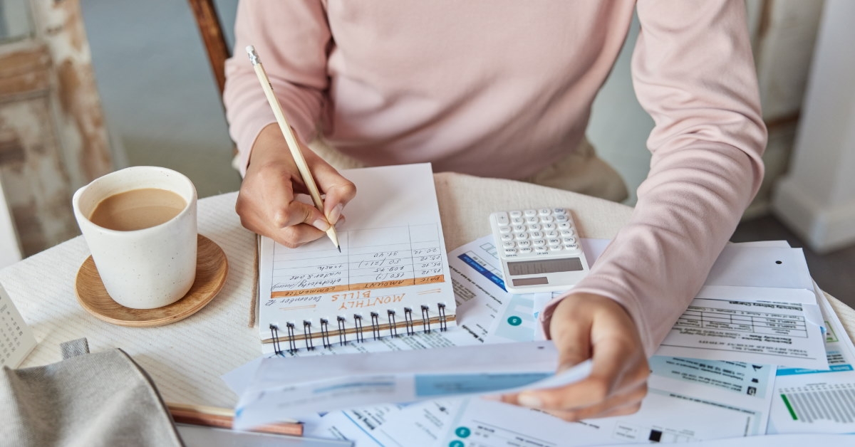 woman sitting at table reveiwing utility bills while making calculations on spiral notebook