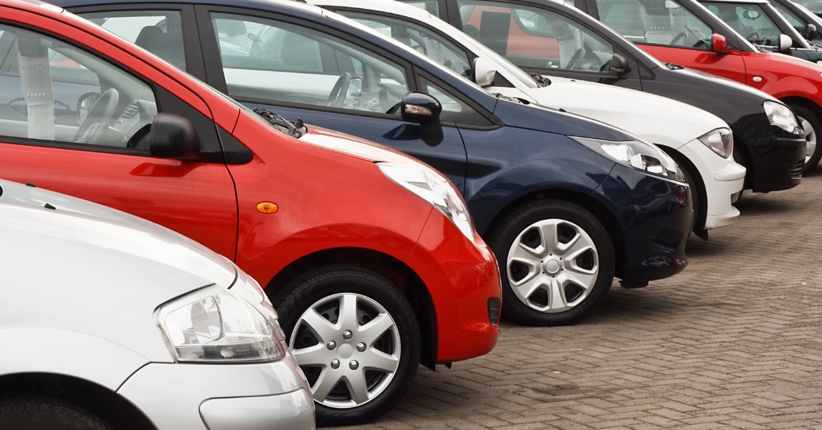cars for sale standing in rows outside car dealership showroom during day time