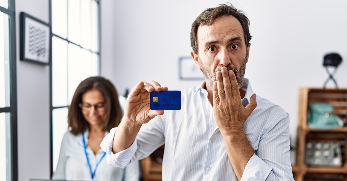 man holding card in hand while covering mouth in shock at retail shop