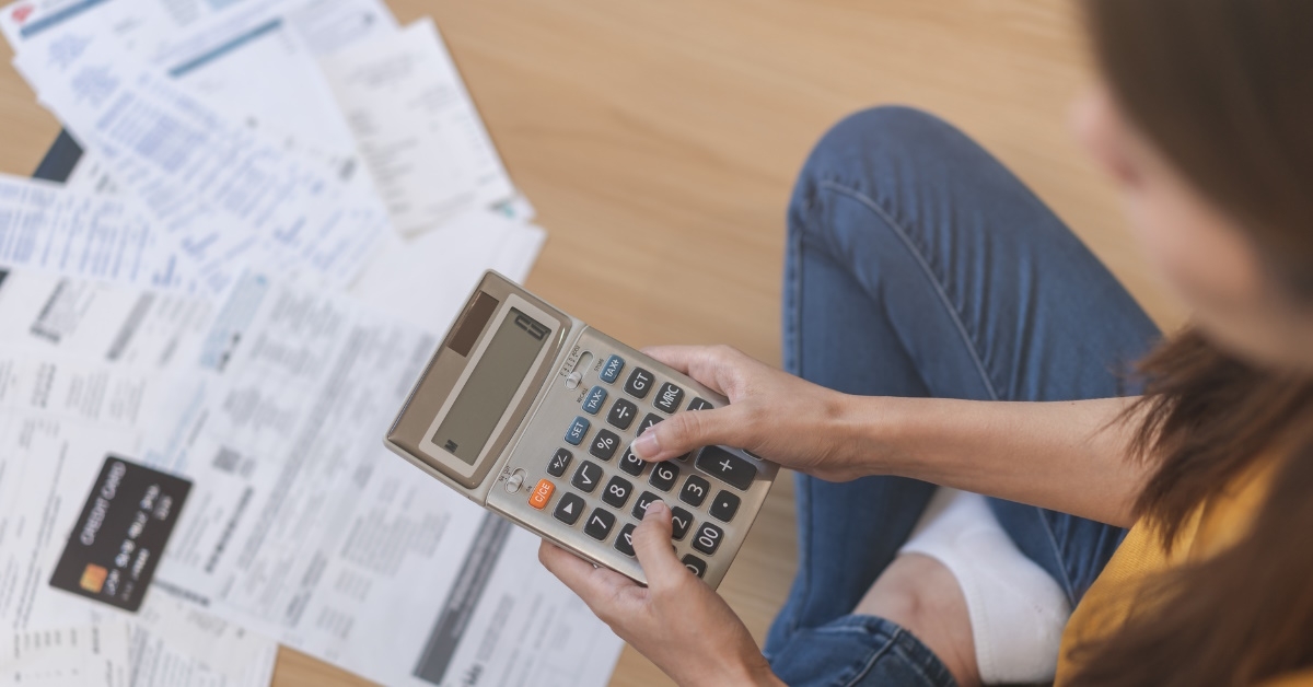 woman sitting on floor with pile of bills using calculator to calculate budget