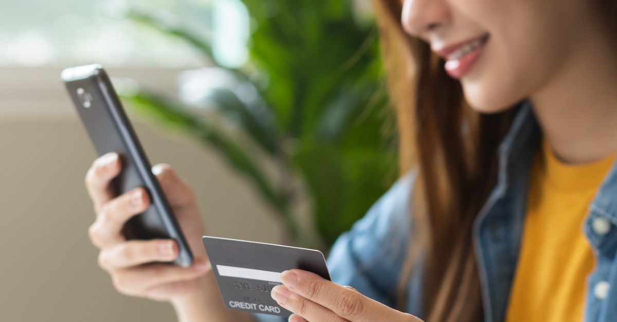 woman holding card in hand while doing online shopping using smartphone