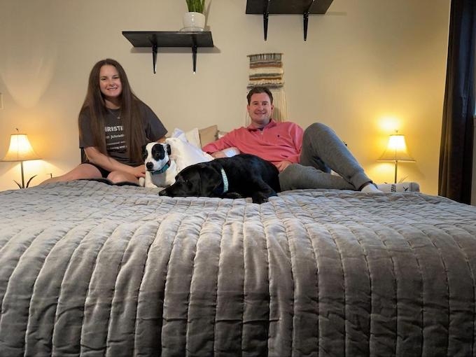 Christine and Seth sitting on their bed. Their two dogs are laying between them. 