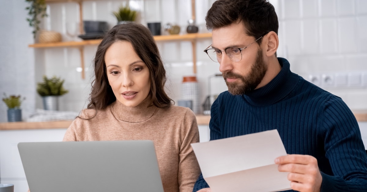 couple sitting at table reviewing bills while using laptop