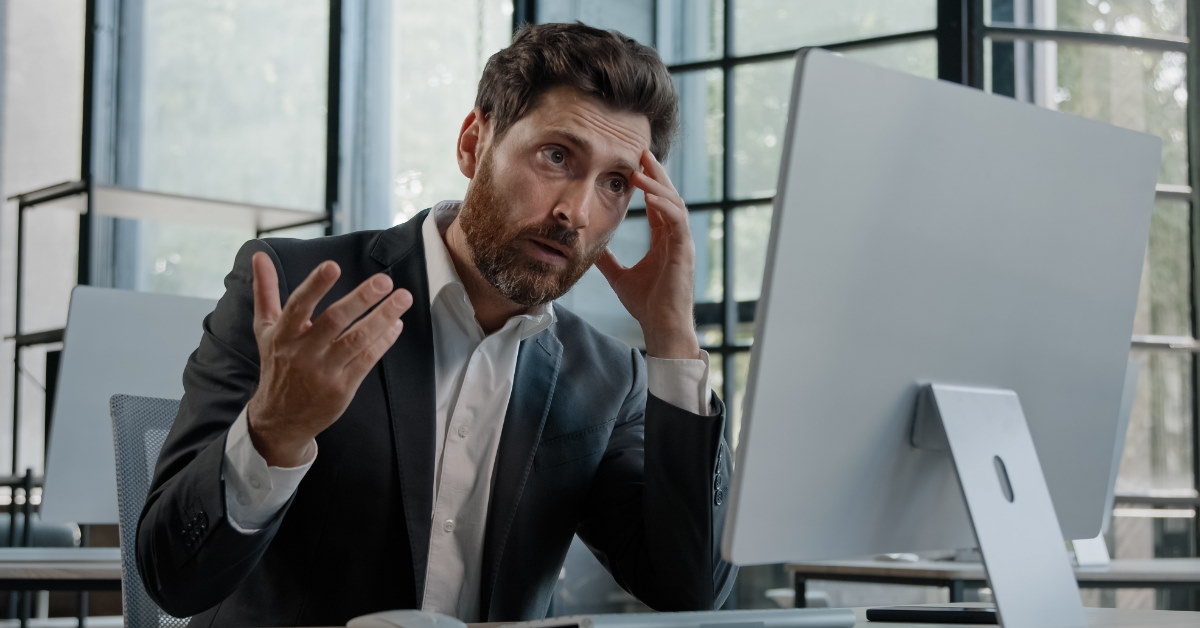mature man in suit shocked in front of desktop computer
