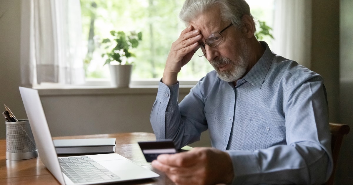 senior man looking at card in stress while using laptop