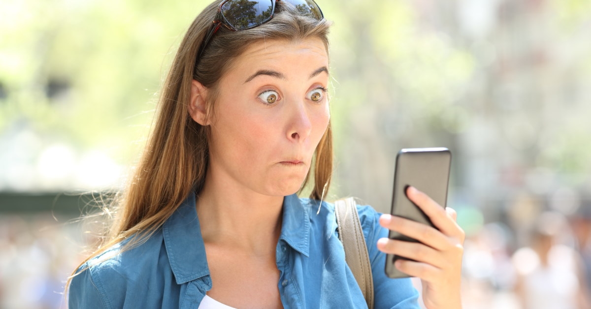 woman shocked while looking at phone screen outside.