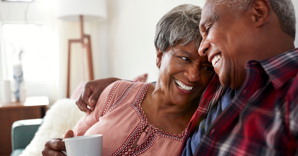 loving senior couple sitting on sofa at home relaxing with hot drink