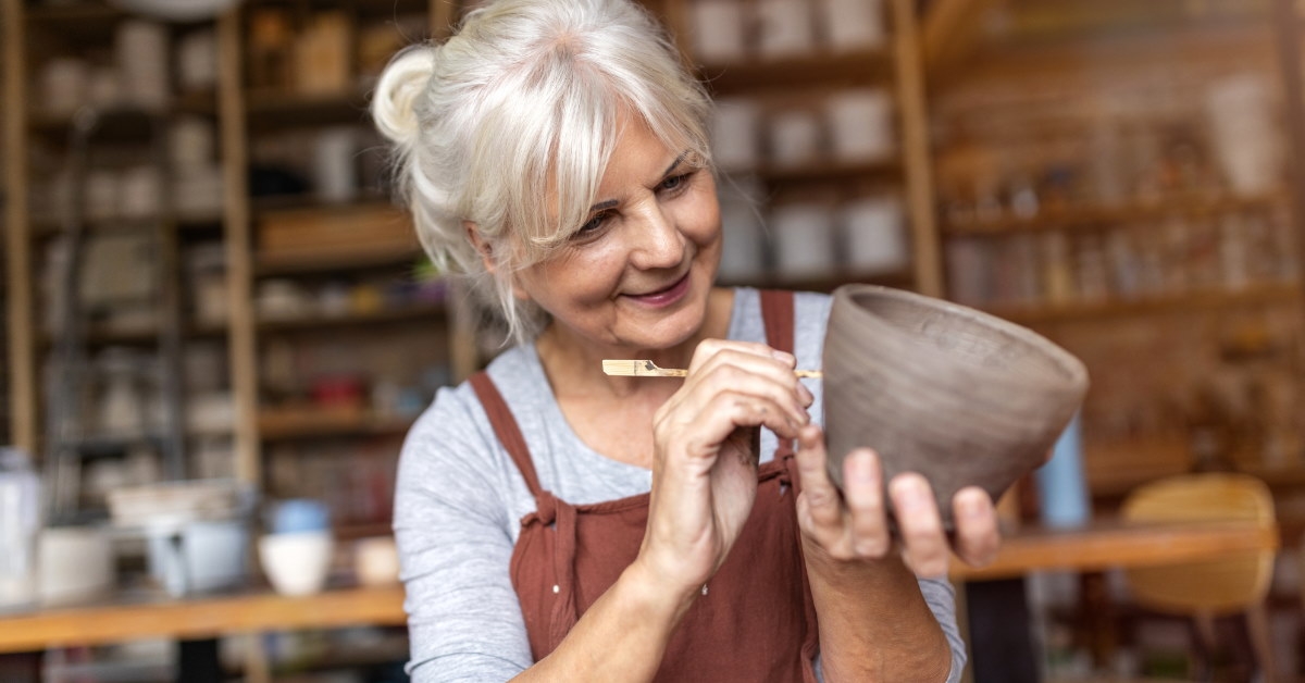 senior female pottery artist holding clay pot using chisel to decorate it