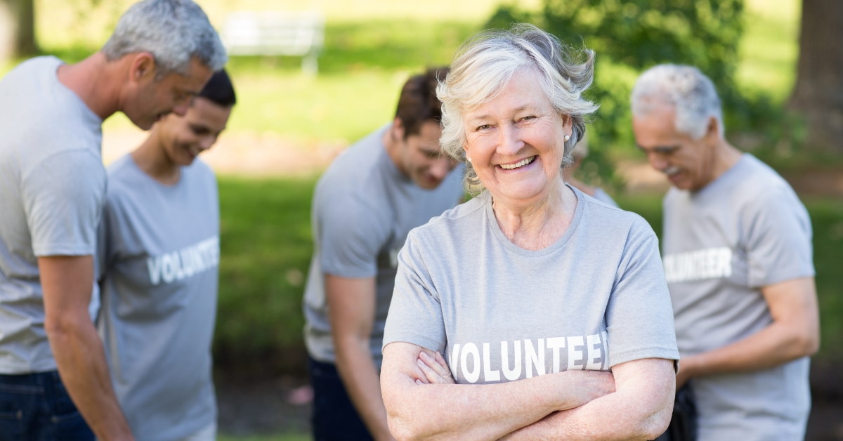 senior woman along with other people in background posing for picture while wearing grey shirts