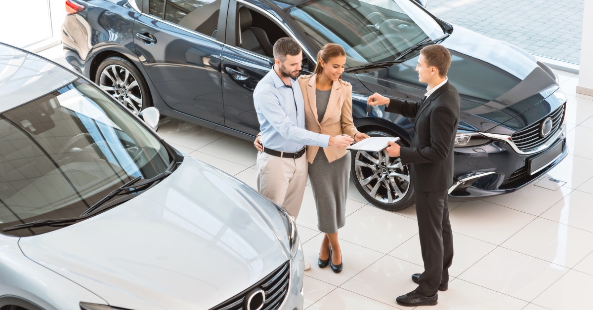 couple standing in car showroom reviewing contract presented by male sales manager