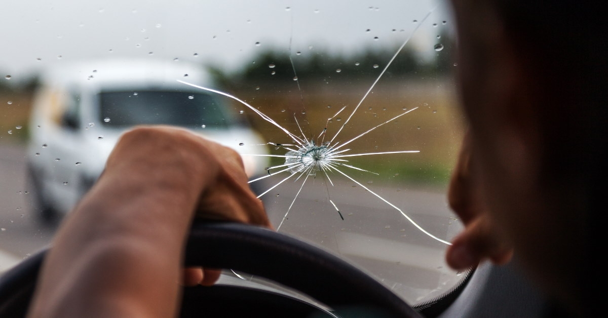 man driving car while sitting in car having broken windshield