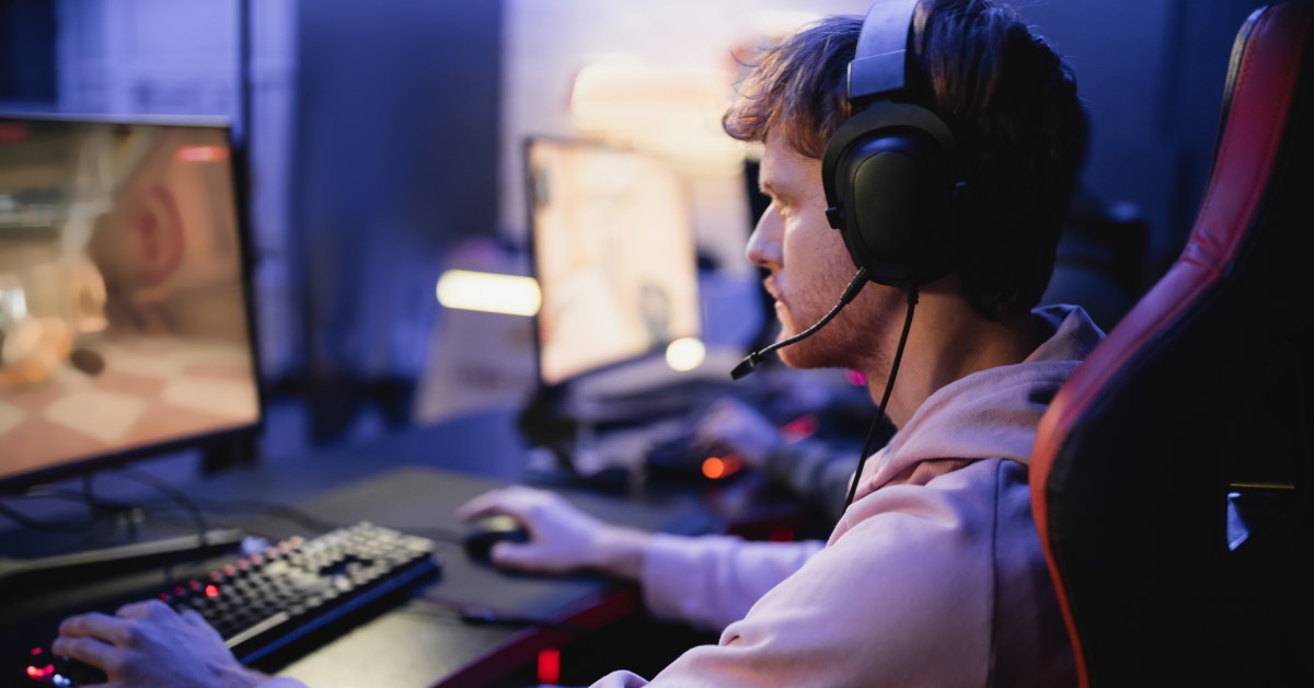 man sitting at table playing game on desktop computer while wearing headset