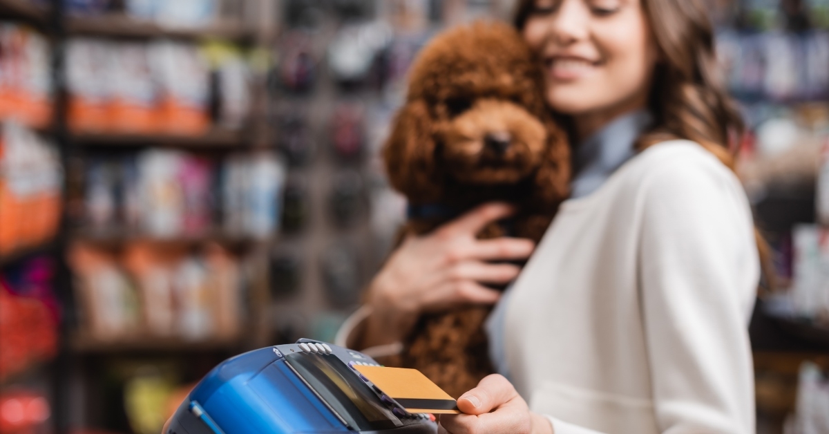woman holding poodle and paying with credit card in pet shop