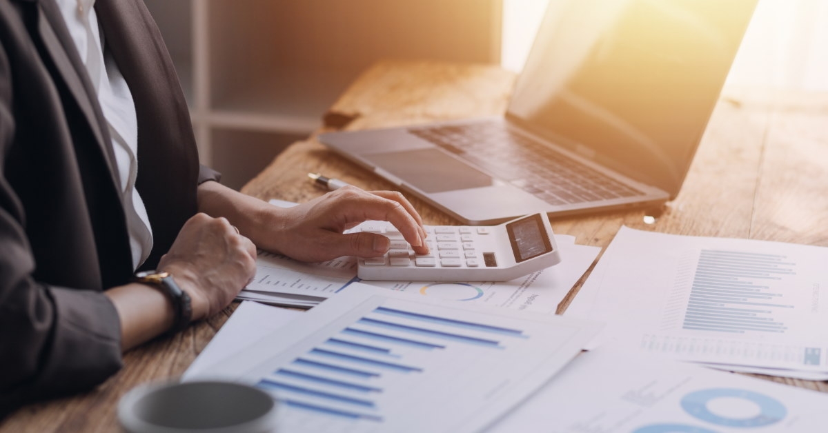 female accountant using calculator at table besides laptop and documents