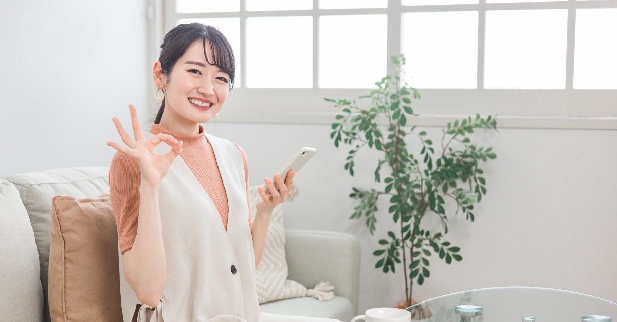 asian woman showing an okay sign while holding a phone