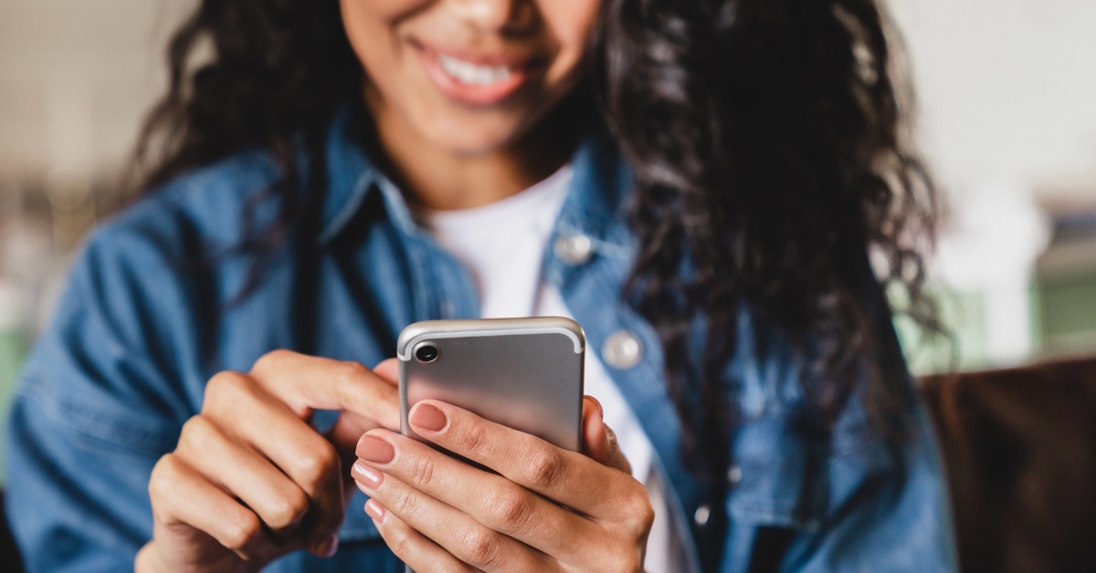 young african american woman wearing denim jacket smiling while using smartphone at home