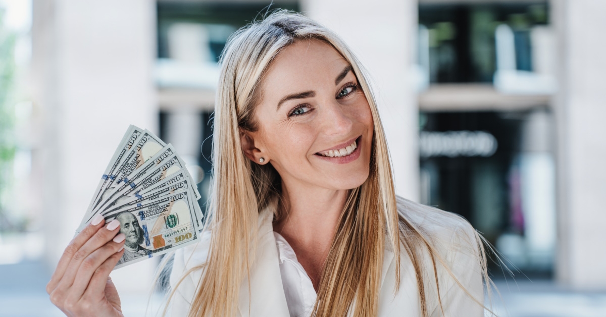 attractive business woman smiling while standing outdoor flaunting dollars in hand