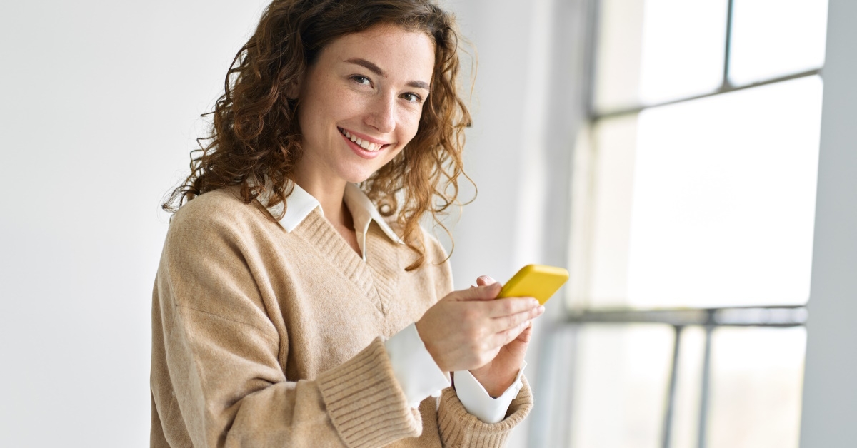 beautiful woman smiling while holding smartphone in hand