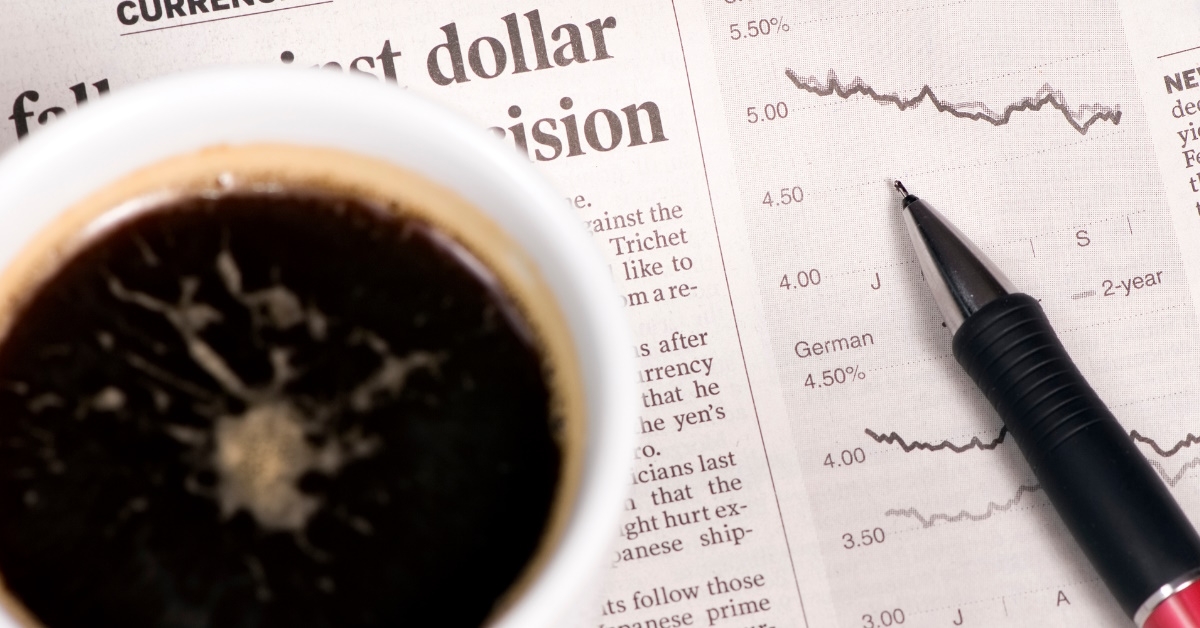 cup with black coffee and pen placed over newspaper with bond yield charts