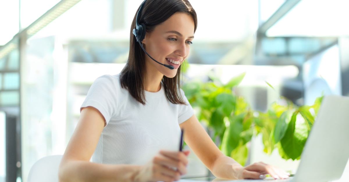 female customer support agent wearing headset talking to client while sitting in call centre