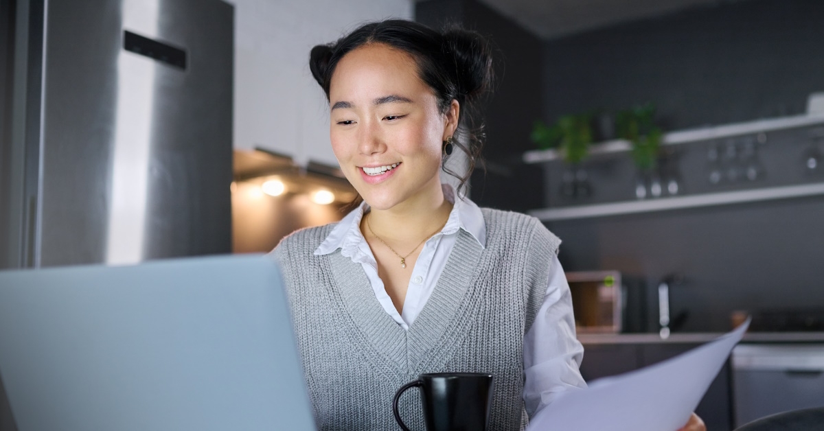 happy asian female accountant sitting at office reviewing papers while using laptop