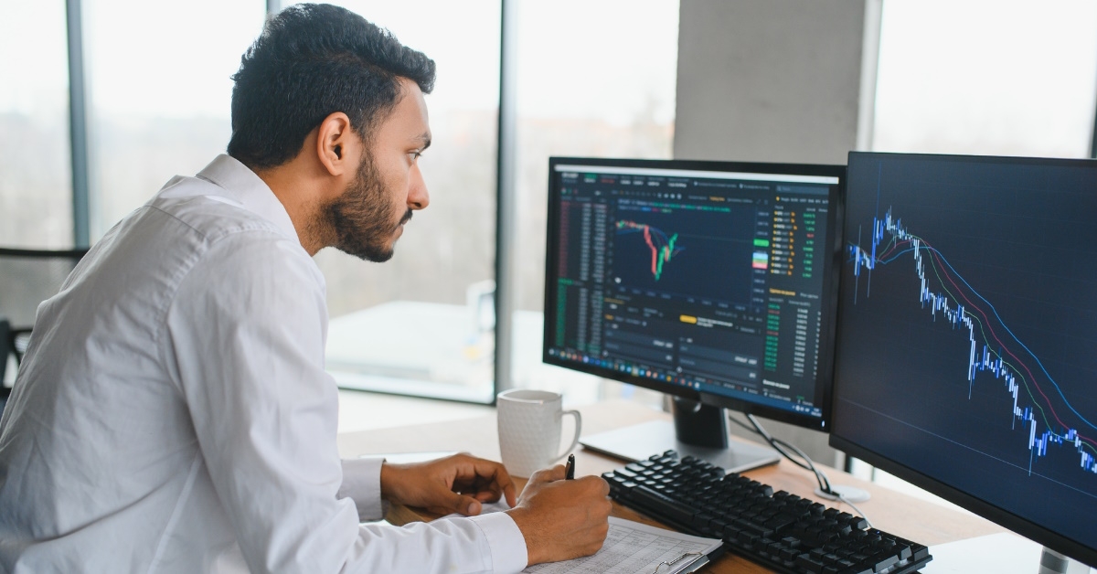 male broker looking at screen while reviewing stock graphs