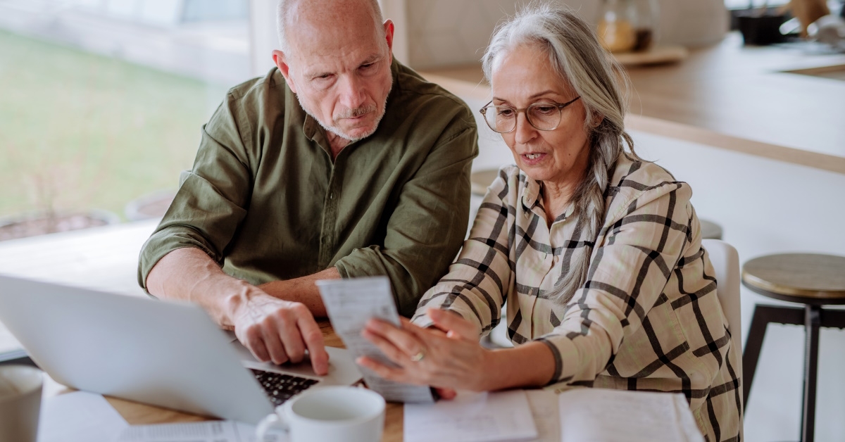 senior couple sitting at table using laptop while calculating expenses together
