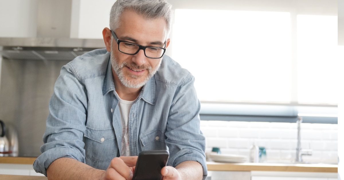 man using smartphone while leaning at wooden countertop in kitchen