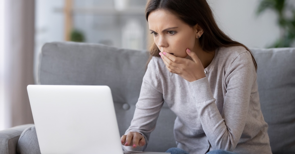 woman sitting in front of laptop covering mouth in shock