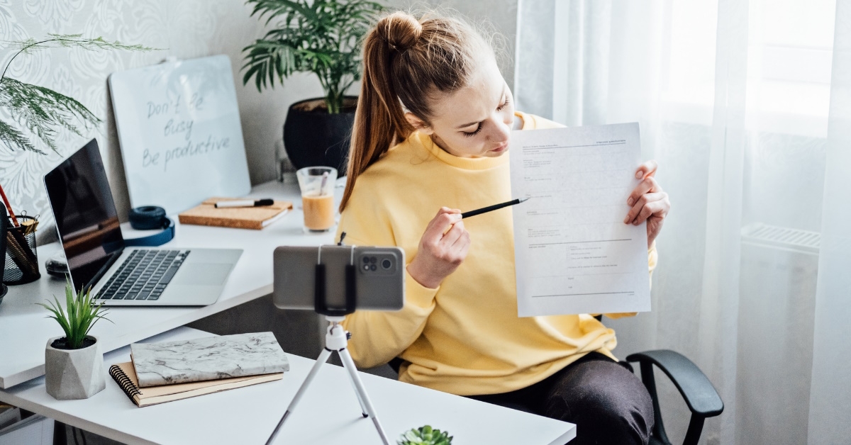 woman using pen to show papers in front of smartphone while vlogging at work