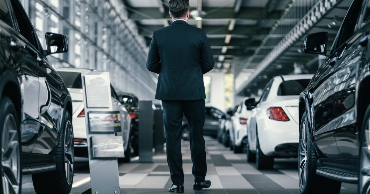 male sales manager wearing suit walking through rows of cars at car dealership showroom