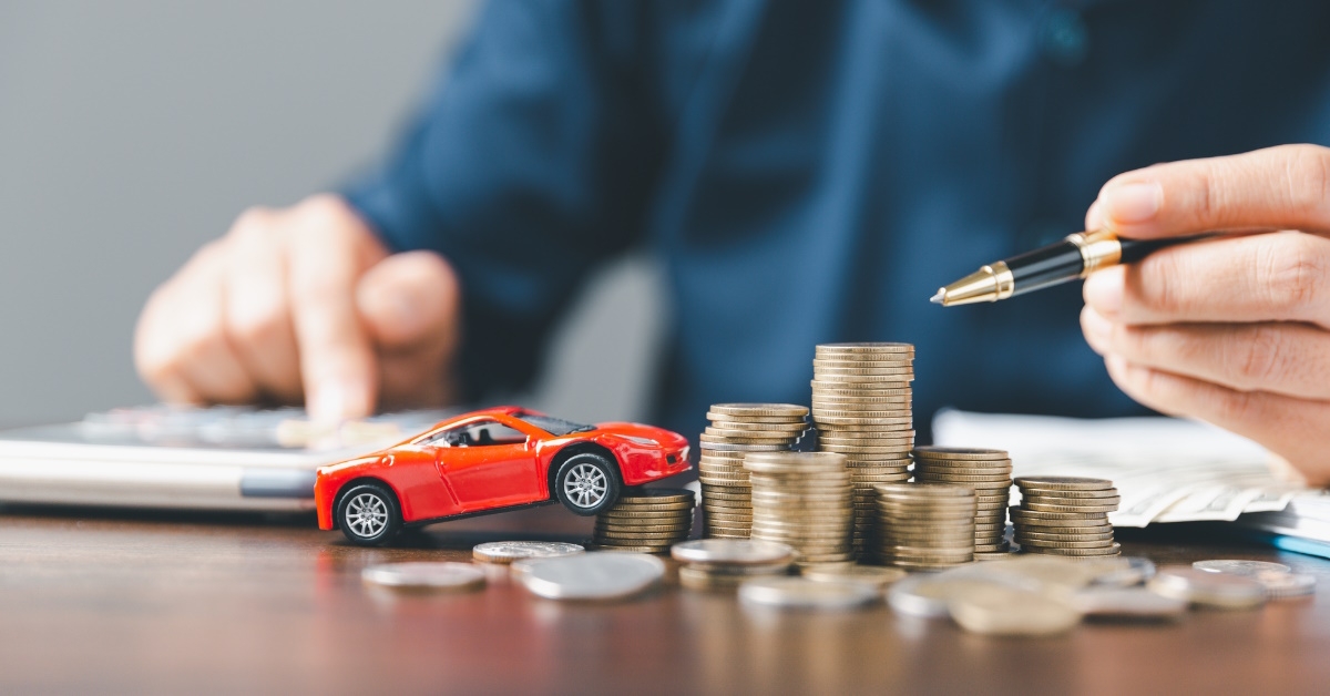 man sitting at table using pen to count pennies on table using calculator besides red toy car