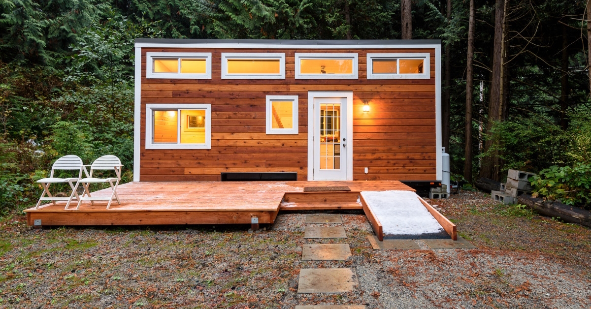 small wooden house with chairs on deck in woods during day time