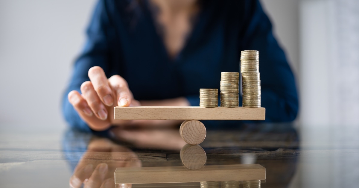 businesswoman sitting on table at office balancing stack of coins on wooden seesaw
