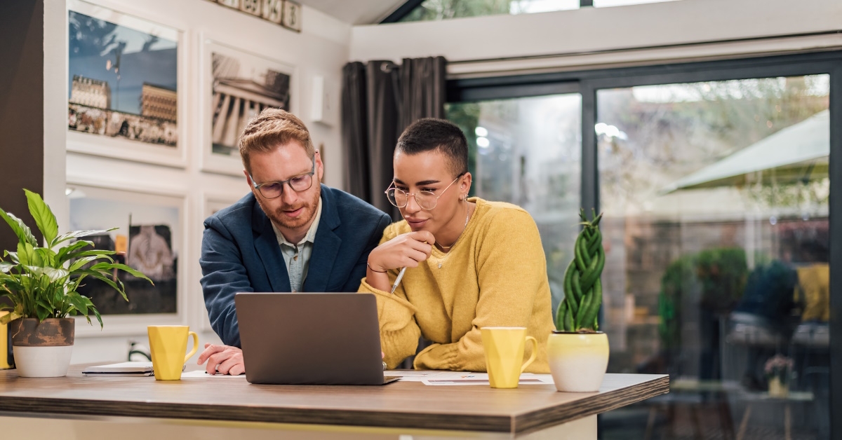multi ethnic couple leaning towards laptop for work in lounge
