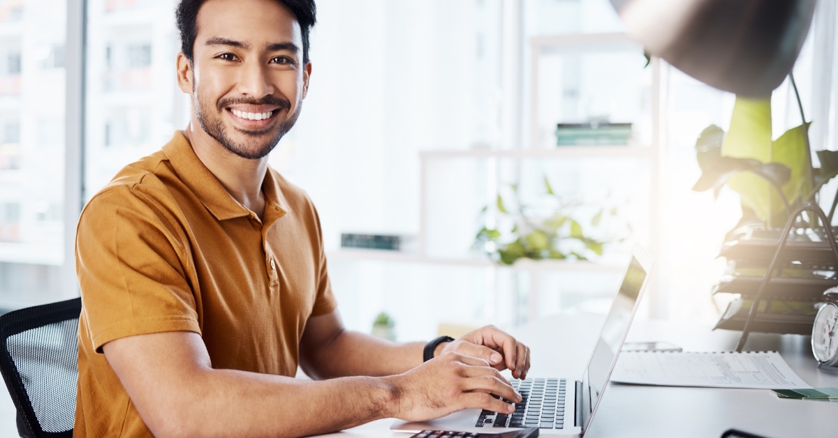 happy man posing at camera while working on laptop at office
