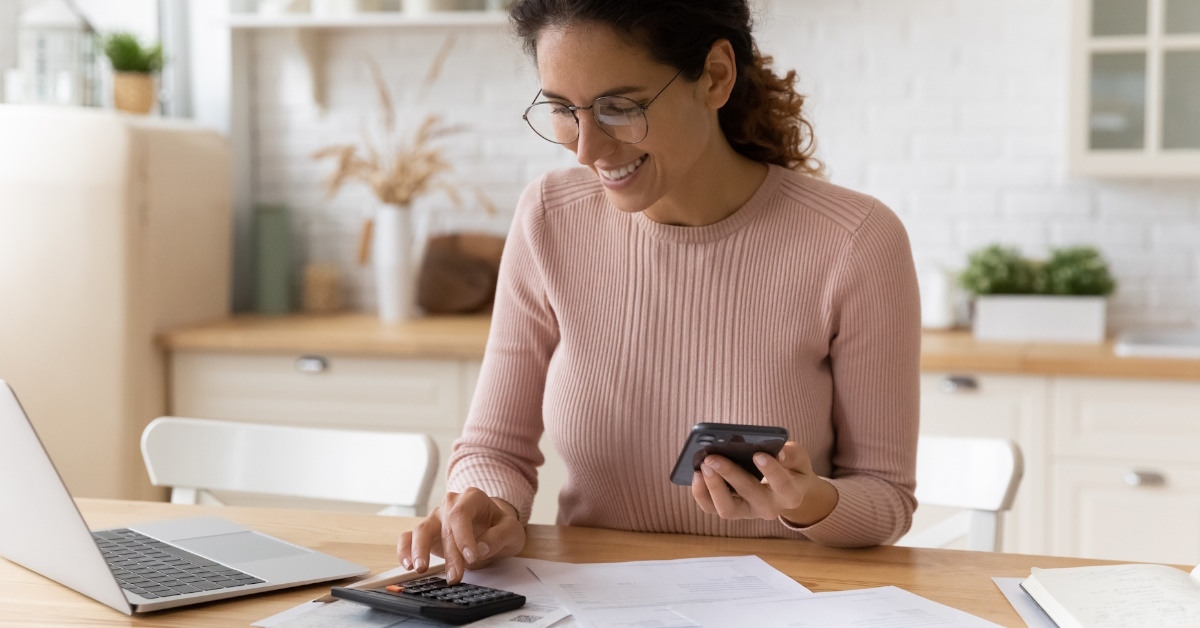 woman calculating bills using calculator while holding smartphone