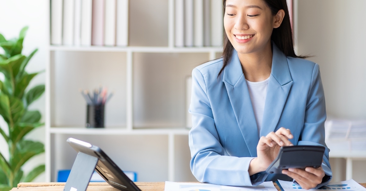 asian business woman in suit using calculator while looking at tablet on table