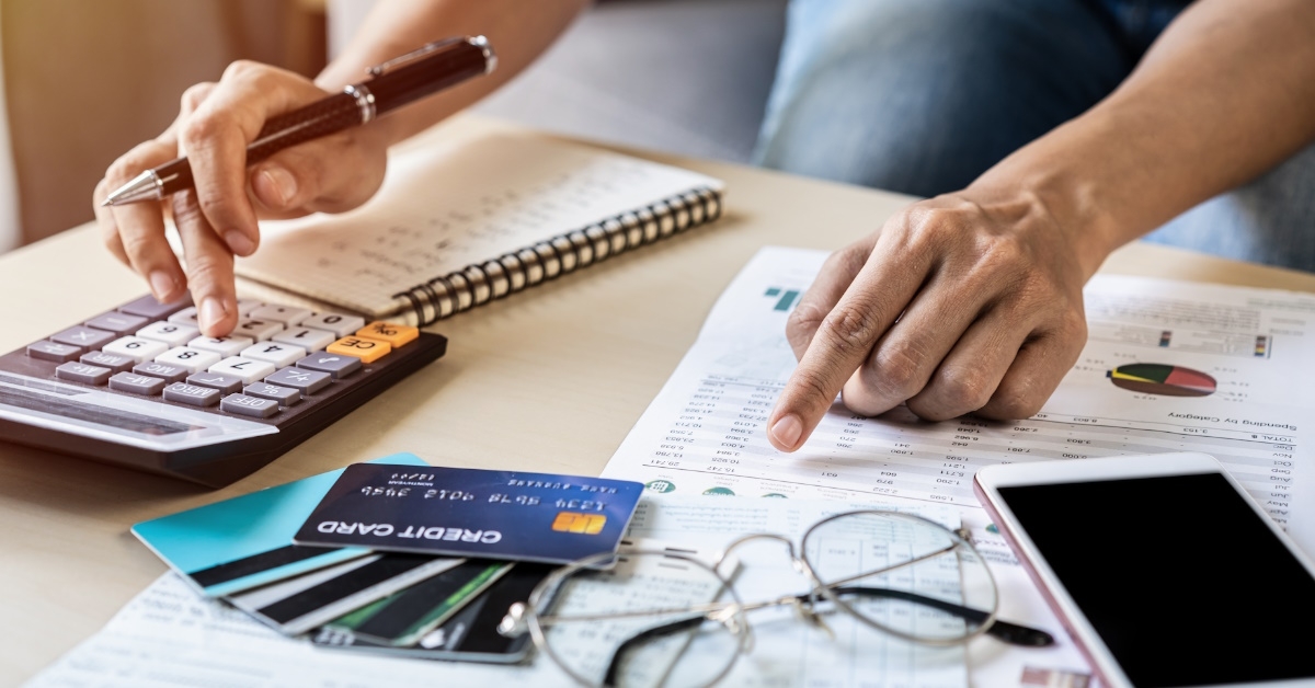man sitting at table writing expenses while calculating budget using calculator 