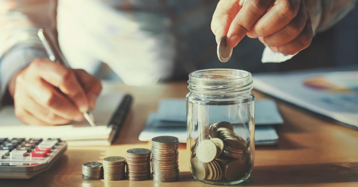 man putting pennies into glass jar at table while writing about it