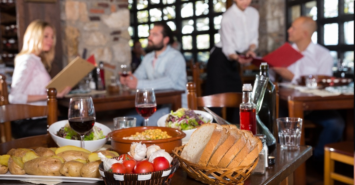 table full of food at restaurant with guests and waitress in background