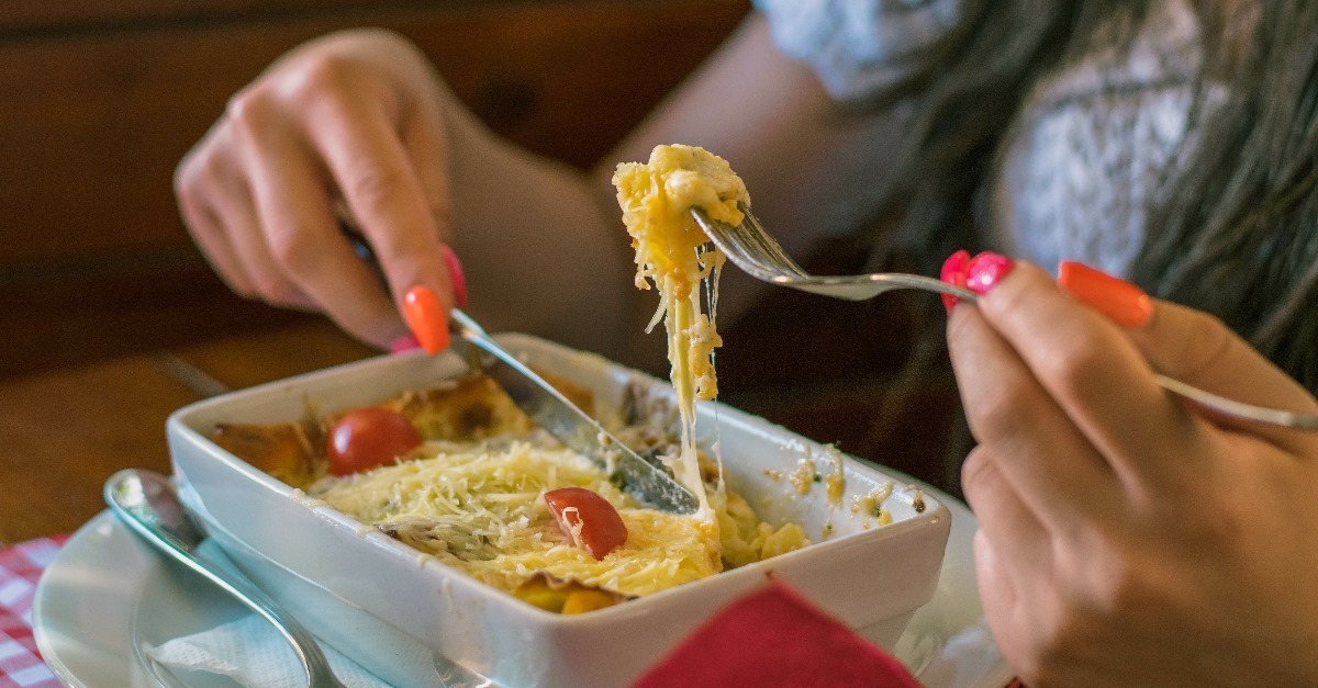 woman holding fork and knife to eat lasagna out of bowl