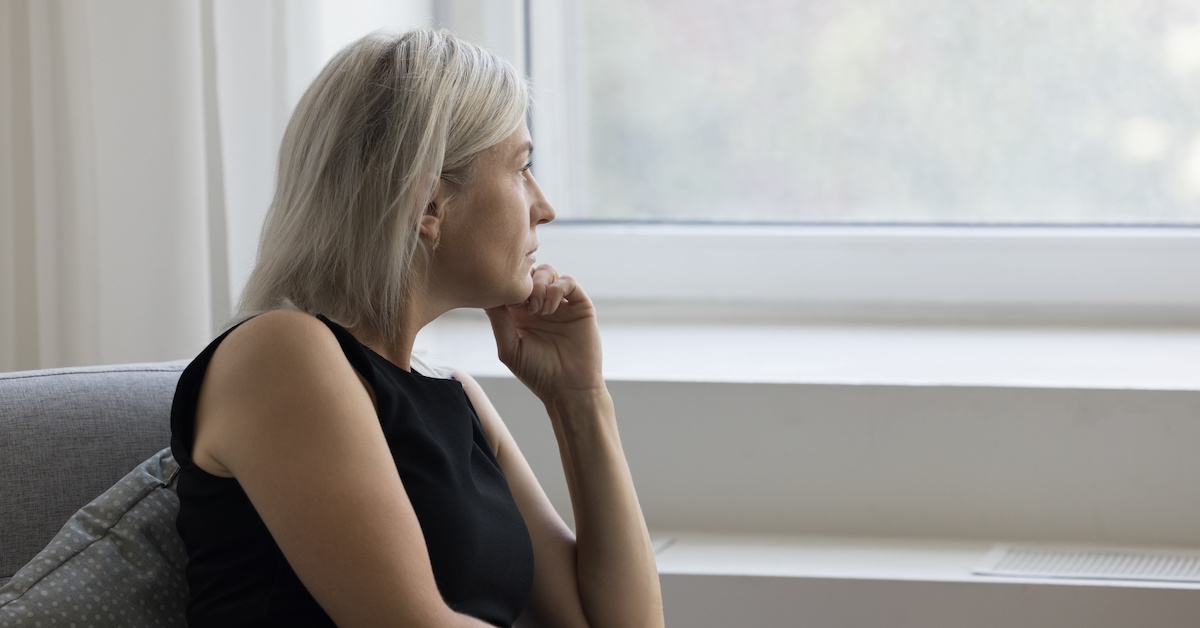 An older woman looks out the window in her home